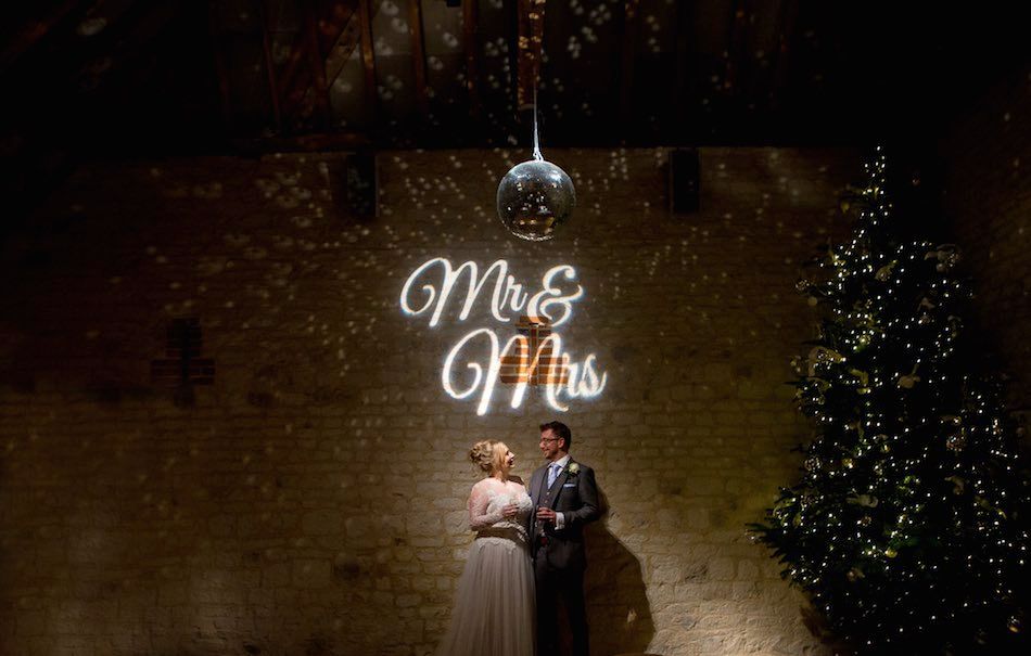 Hannah and Mike under the Mr and Mrs sign at Bury Court Barn next to the Christmas tree - Photography by Em J Photo and Videography by Veiled Productions
