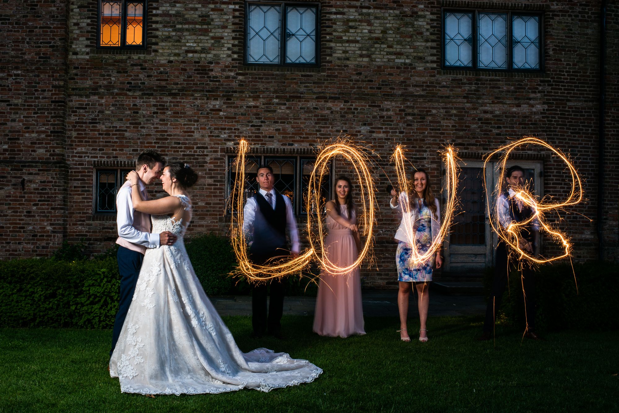Abbie and Brett stood in front of Old Hall in Ely whilst their friends spell 'LOVE' with sparklers. Photo thanks to Ryan Jarvis Photography.