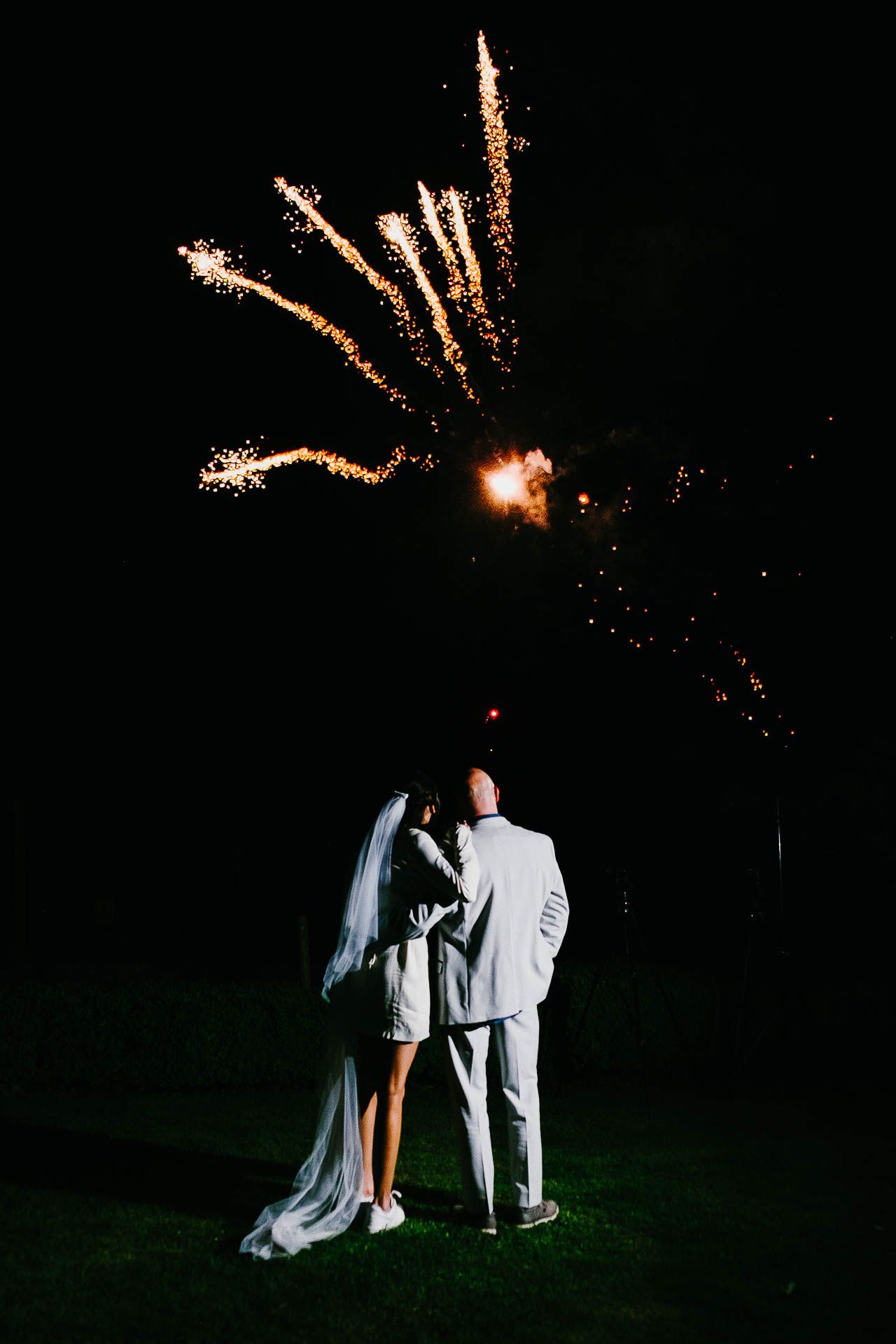 Bright sparks shoot into the night sky as Adrian and Nadia watch with their backs to the camera. Mark Cairns - a mind reader and magician entertainer for weddings and events - wowing guests with his tricks during Adrian and Nadia's wedding reception. Photo by Des Dubber Photography, videography by Veiled Productions