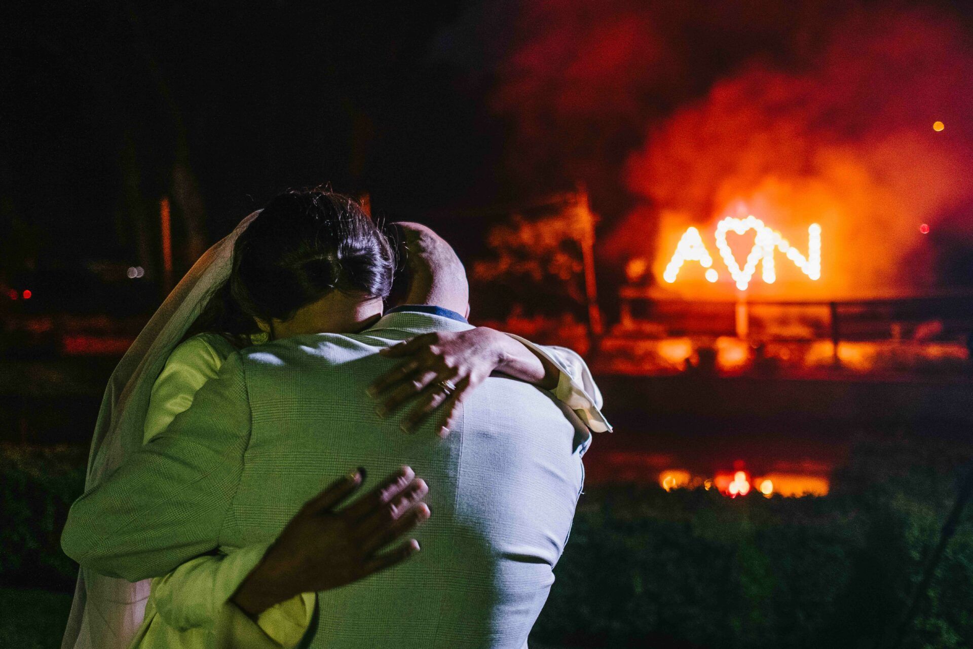 Adrian and Nadia embrace in a heartfelt hug whilst an 'A', a heart and an 'N' are lit up by fire in the background. Mark Cairns - a mind reader and magician entertainer for weddings and events - wowing guests with his tricks during Adrian and Nadia's wedding reception. Photo by Des Dubber Photography, videography by Veiled Productions