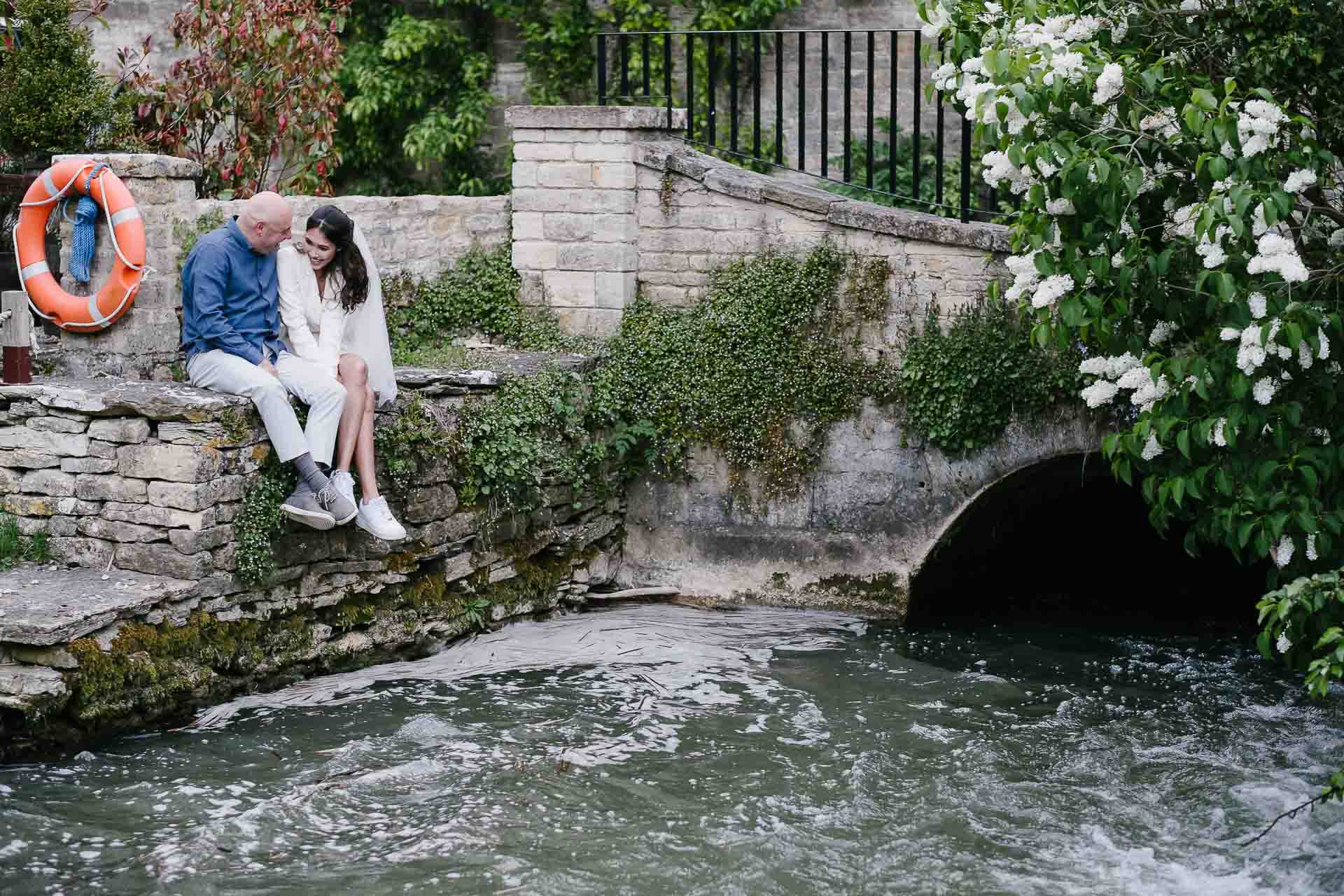 Adrian and Nadia laughing whilst sitting on the edge of bridge at Minster Mill. Photo by Des Dubber Photography, videography by Veiled Productions