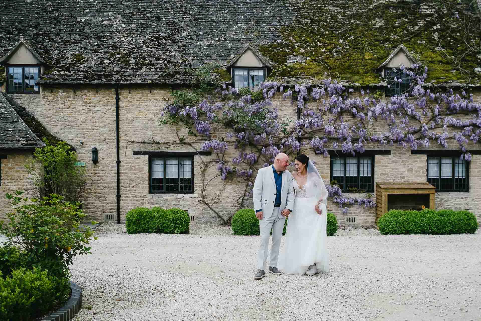  Adrian and Nadia walking towards the camera laughing in fron of the wisteria hanging across the buildings at Minster Mill. Photo by Des Dubber Photography, videography by Veiled Productions