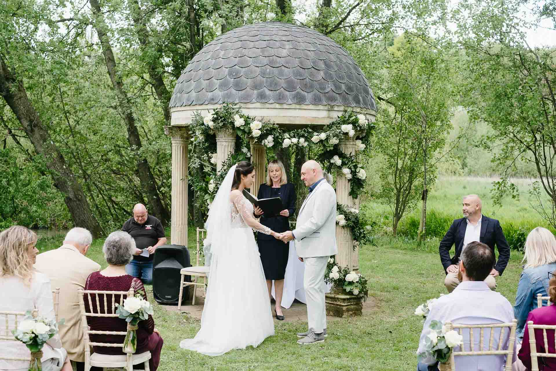 Adrian and Nadia hand in hand during their ceremony at Minster Mill surrounded by their guests. Photo by Des Dubber Photography, videography by Veiled Productions