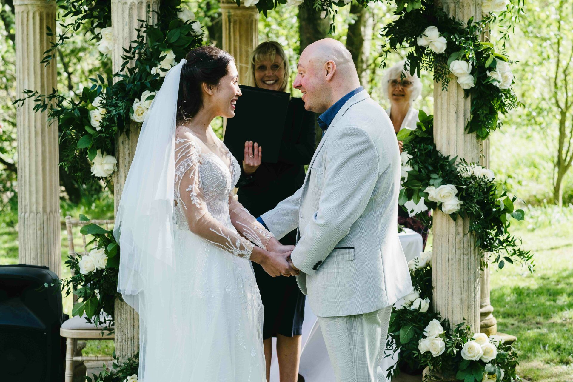 Adrian and Nadia hand in hand in front of Fiona, the registrar as they are announced husband and wife. Both have excited, happy faces. Photo by Des Dubber Photography, videography by Veiled Productions