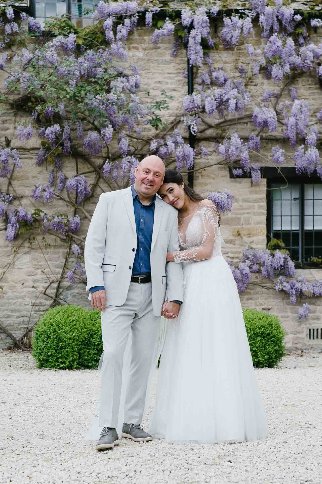 Nadia hugging Adrian during their couple's photoshoot in front of the wisteria hanging across Minster Mill. Photo by Des Dubber Photography, videography by Veiled Productions.