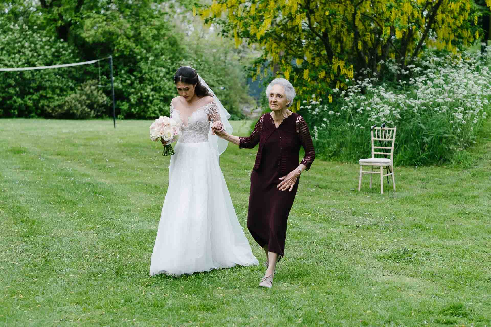 Nadia walking across the gardens of Minster Mill with Adrian's Mum accompanying her holding her hand. Photo by Des Dubber Photography, videography by Veiled Productions