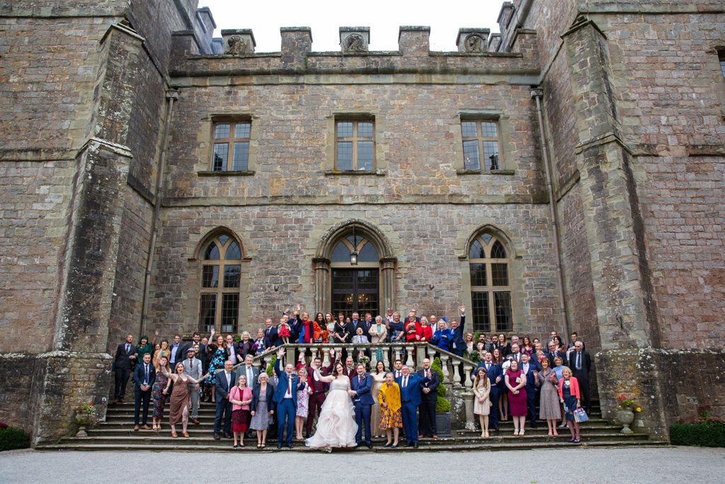 Photo of Aimee and Simon and all of their wedding guests cheering outside of Clearwell Castle. Photo thanks to Mark Lord Photography.