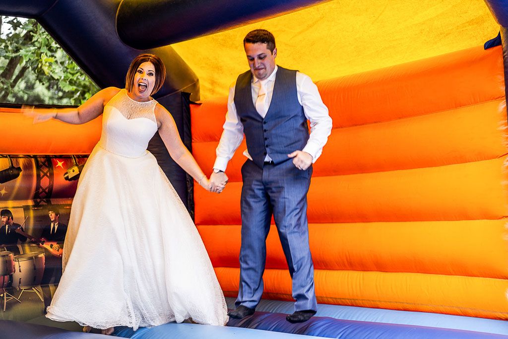 Amy and Mario bouncing on the bouncy castle during their wedding reception. Wedding photo by Allister Freeman. Videography by Veiled Productions - unique wedding videographer Bury Court Barn