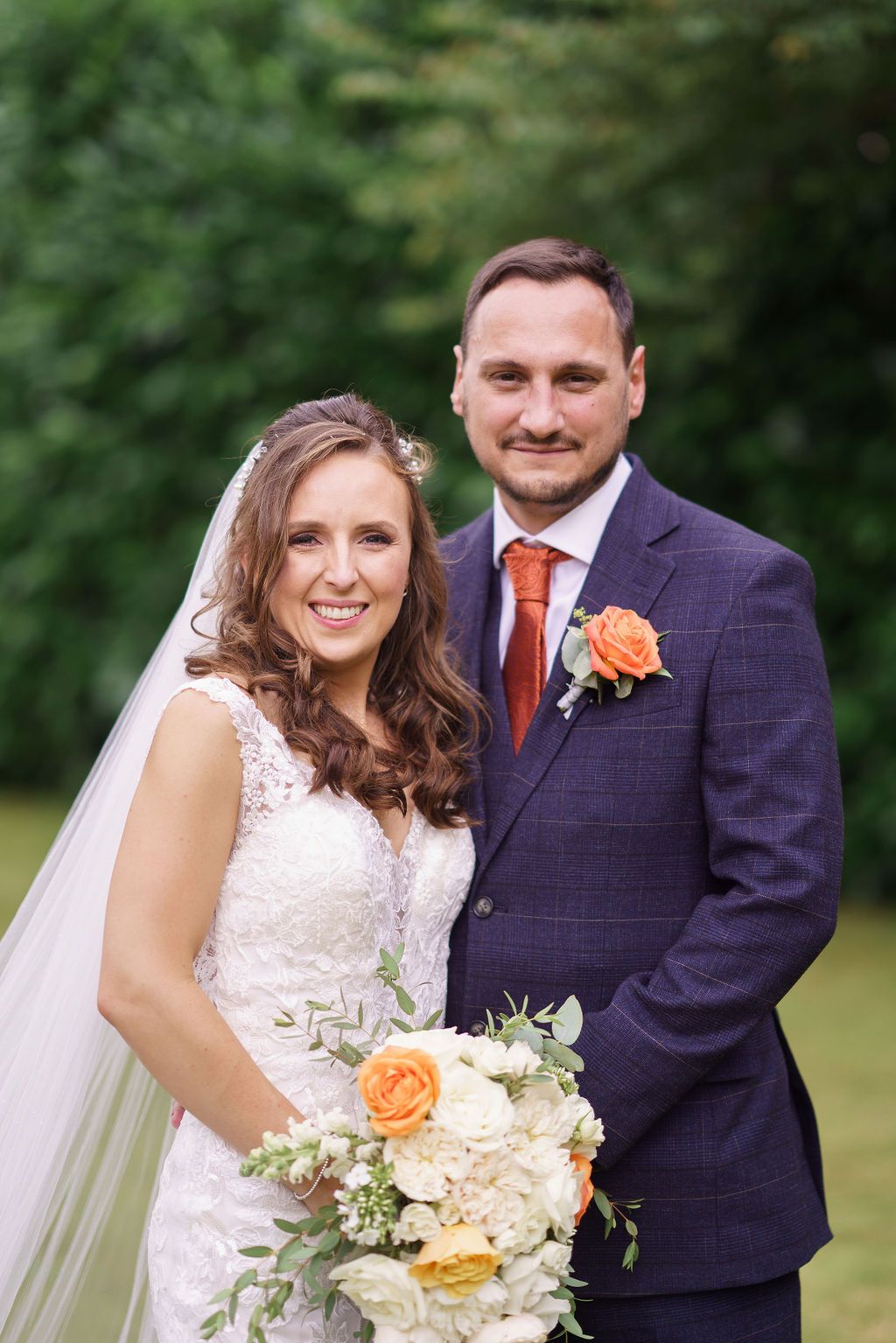 Bex and Dan stand together as newlyweds. Bex holding her bridal bouquet of flowers - photo thanks to J Bidmead Photography