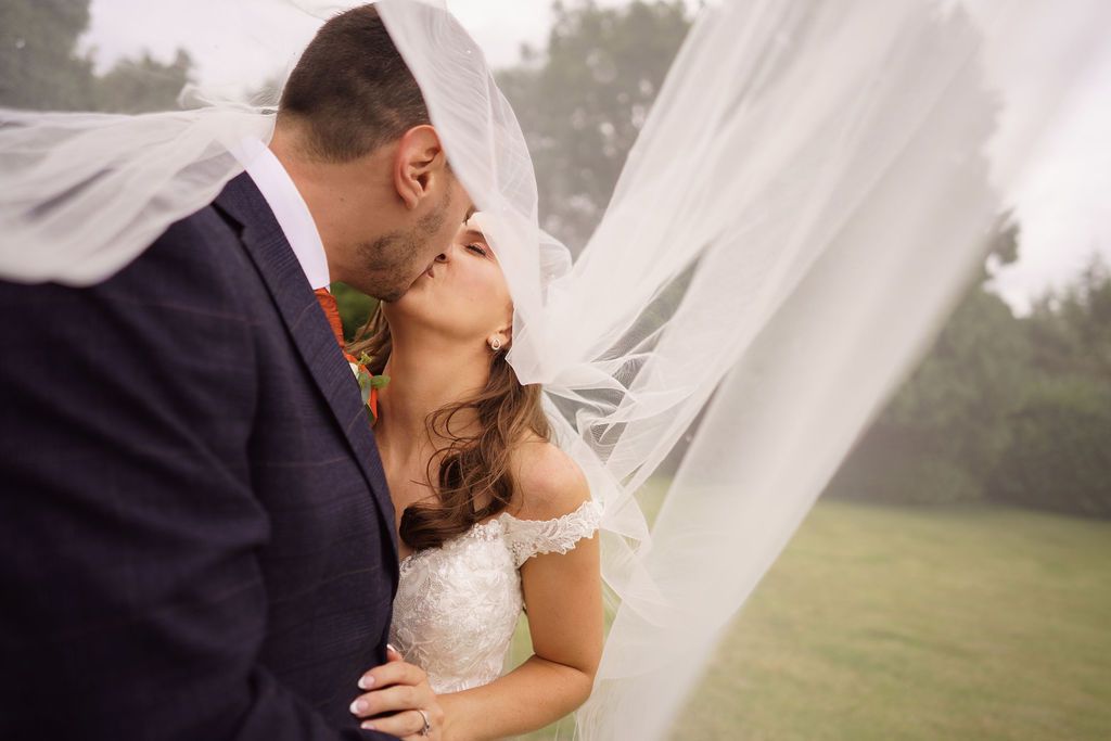 Bex and Dan kiss under Bex's veil - photo by J Bidmead Photography, fun wedding film by Veiled Productions