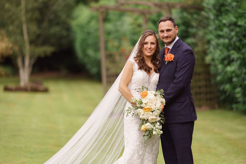 Bex and Dan standing together in the gardens at Redhouse Barn. Photo thanks to J Bidmead Photography