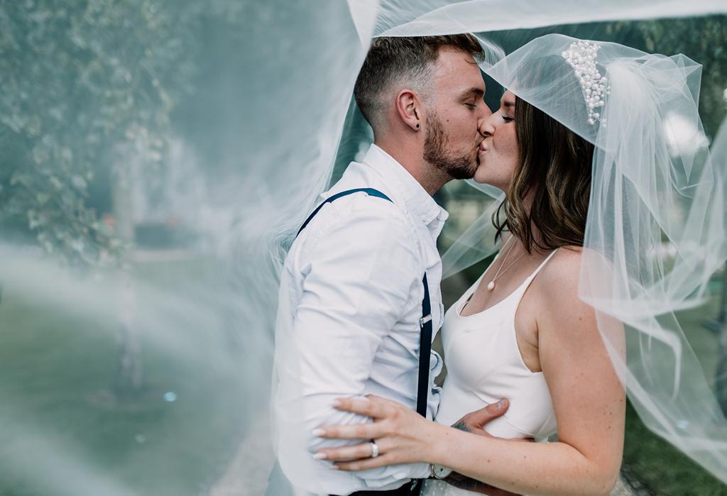 Under the veil Erin and Vinnie kiss on the lawn of The Tythe Barn wedding venue - photography by The Kensington Photographer