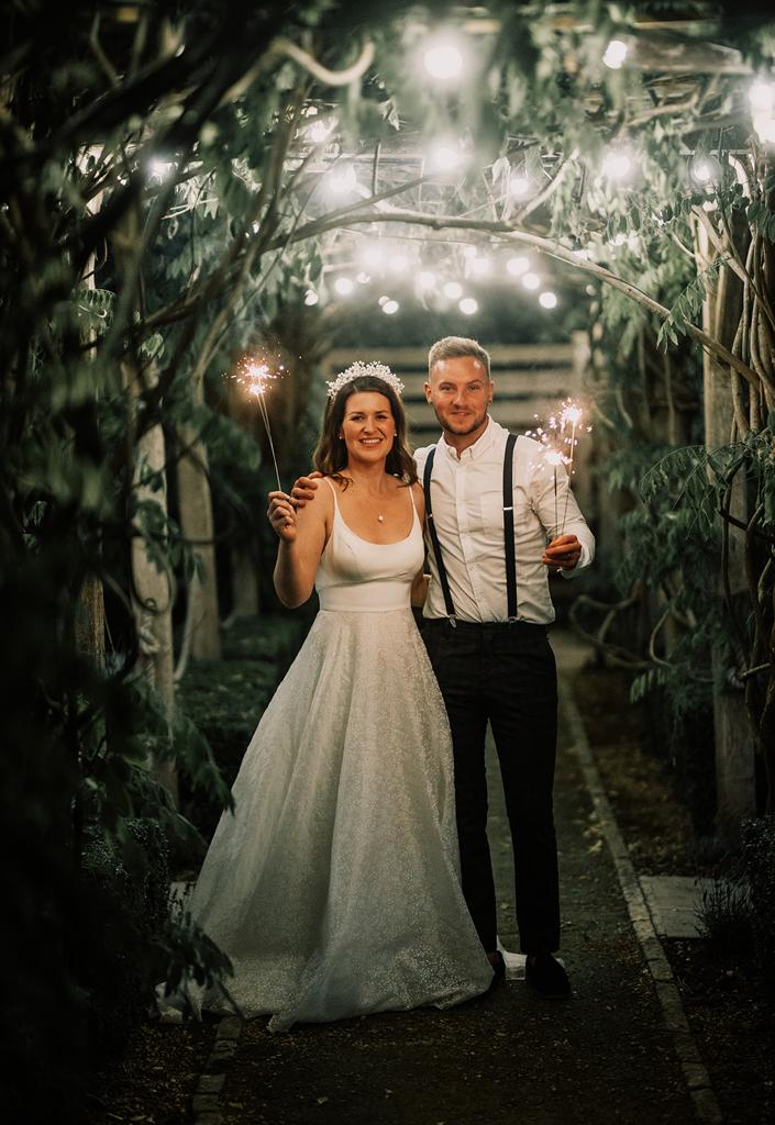 Erin and Vinnie with sparklers under the lights of the courtyard at The Tythe Barn - photography by The Kensington Photographer