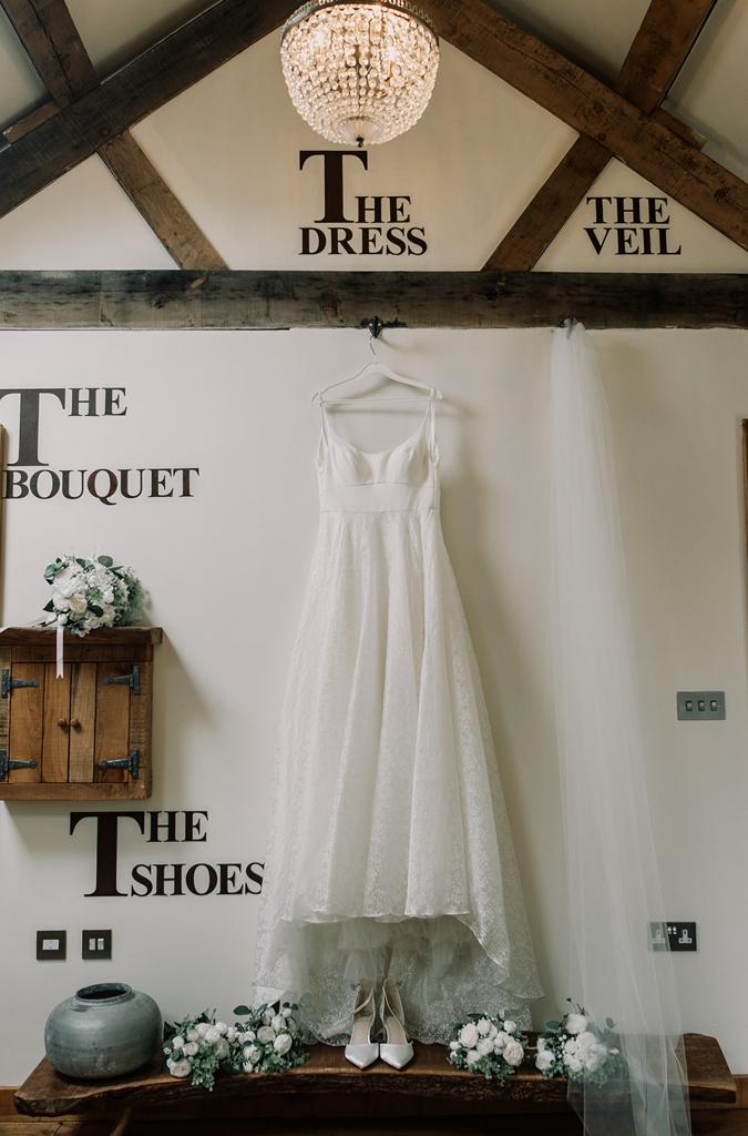 Erin's wedding dress by Sassi Holford hanging in the Nook at The Tythe Barn - photo by The Kensington Photographer