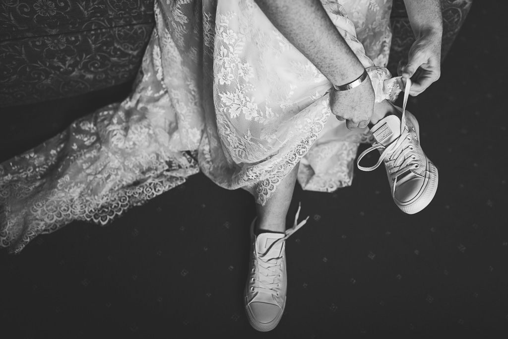 Rachel tying the laces on her wedding day Converse white shoes. Photography by Tiree Dawson Photography. Videography by Veiled Productions. Sophisticated New House Farm wedding in the Summer 2019.