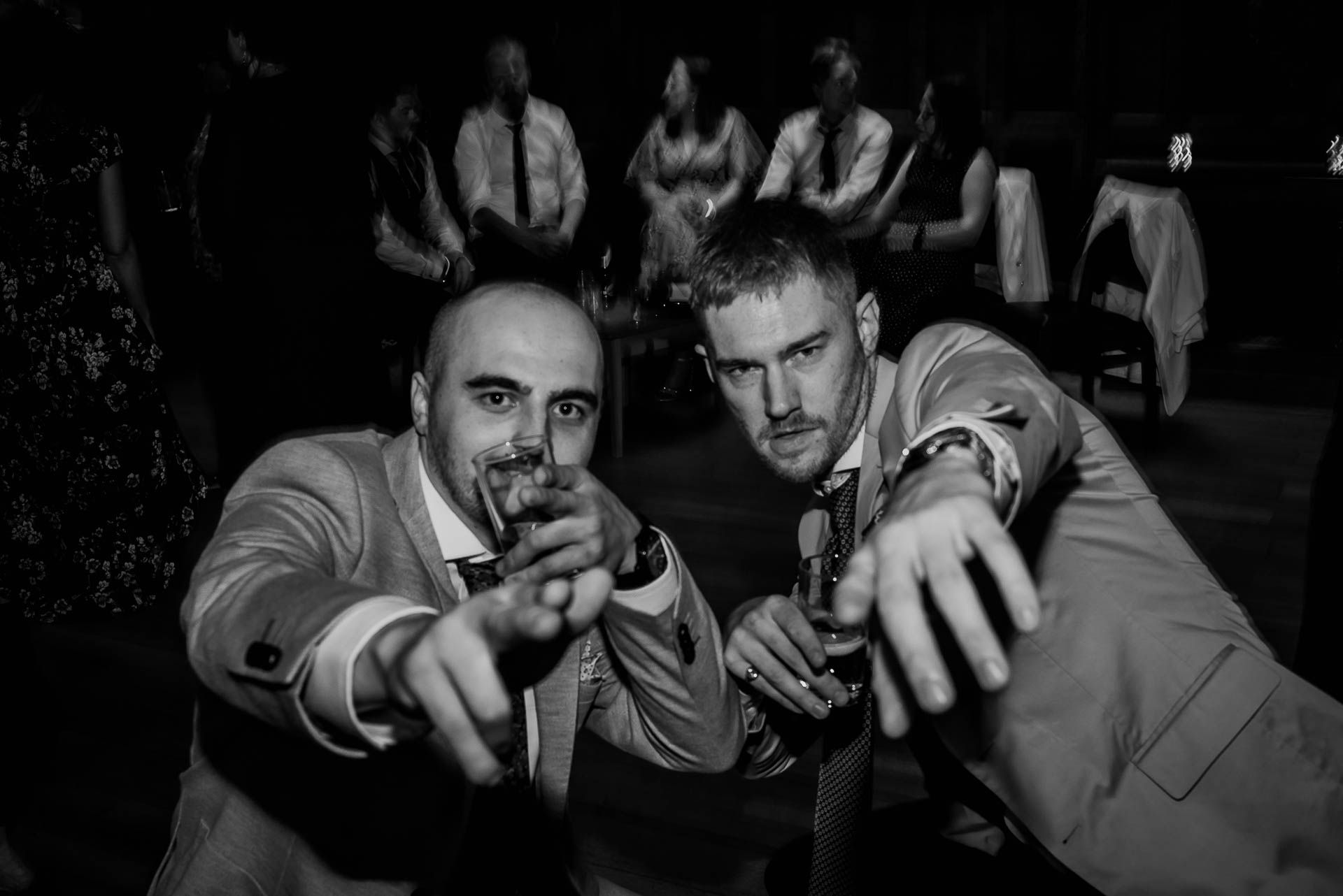 Guests at a wedding pointing at the camera lens whilst dancing on the dancefloor. Black and white photo by Damien Vickers Photography. 