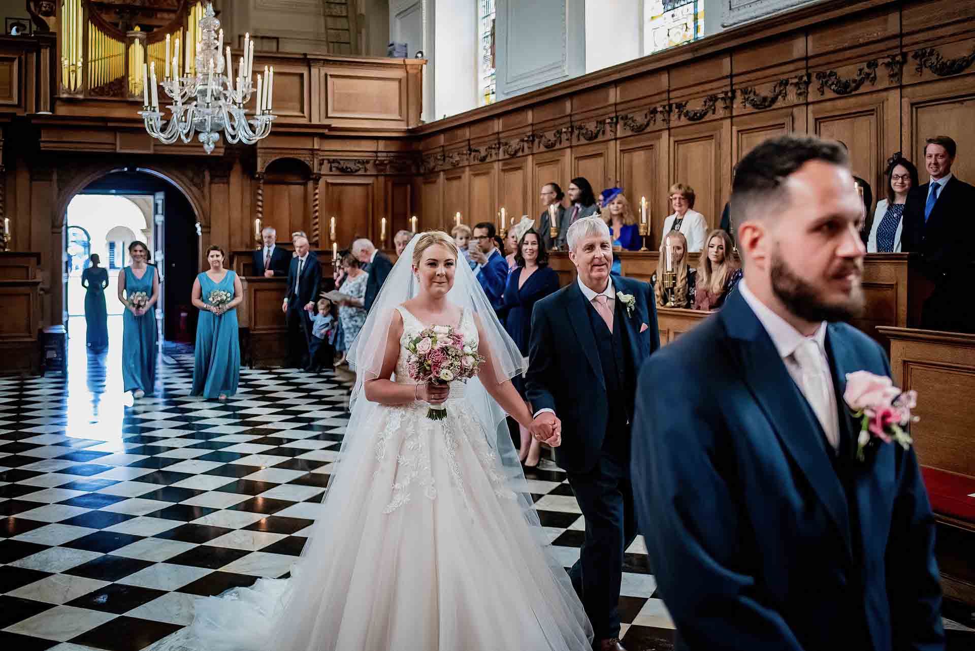 Leah and her Dad walking into the chapel of Emmanuel College in Cambridge with Nic waiting at the top of the aisle. Photo thanks to Damien Vickers Photography. 