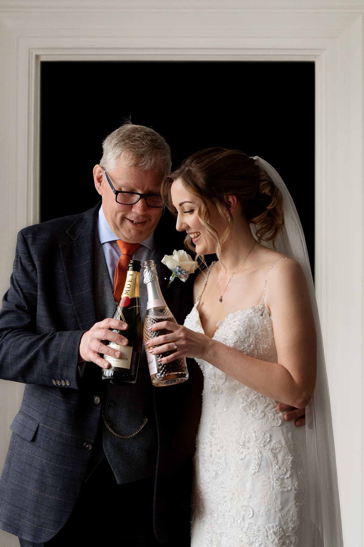 Sophie and her Dad clinking Champagne bottles just before she marries Ross at Swynford Manor. Photo by Fountain Photography.
