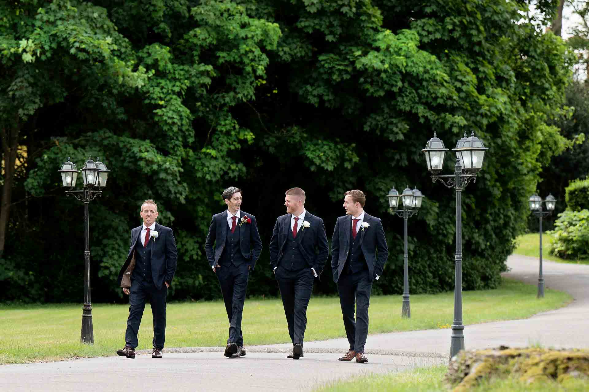 Ross and his groomsmen walking down the drive between lamp posts at Swynford Manor. Photography by Fountain Photography. Videography by Veiled Productions.