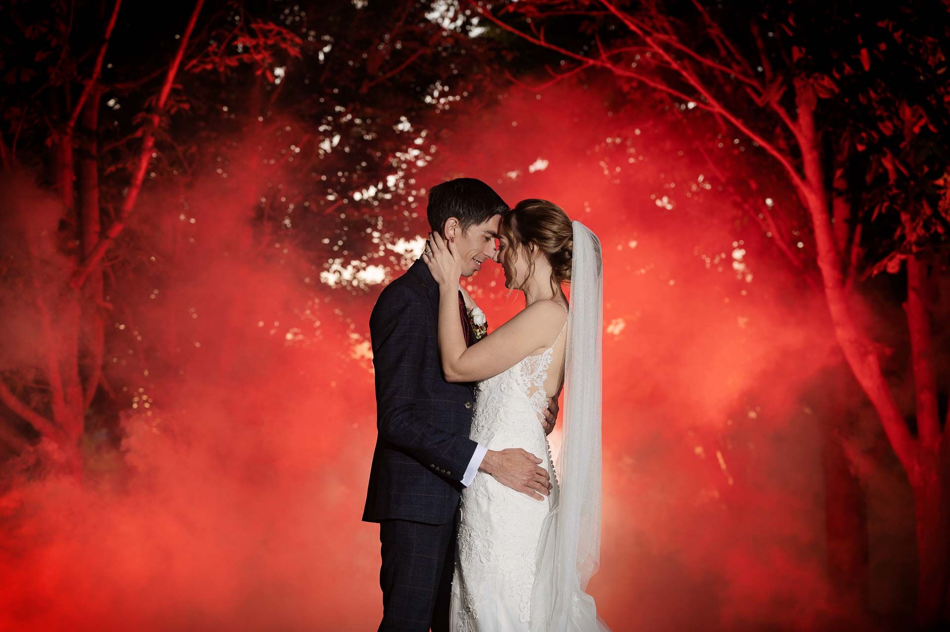 A photo amongst trees with red flash making a smoke bomb look red circulating Ross and Sophie during sunset at Swynford Manor. Photography by Fountain Photography. Videography by Veiled Productions.