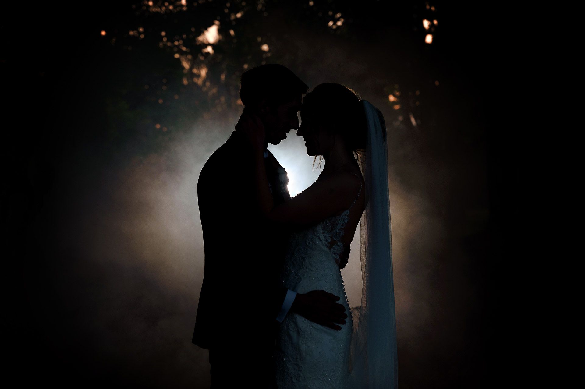 A silhouette photo amongst trees with a smoke bomb circulating Ross and Sophie during sunset at Swynford Manor. Photography by Fountain Photography. Videography by Veiled Productions.