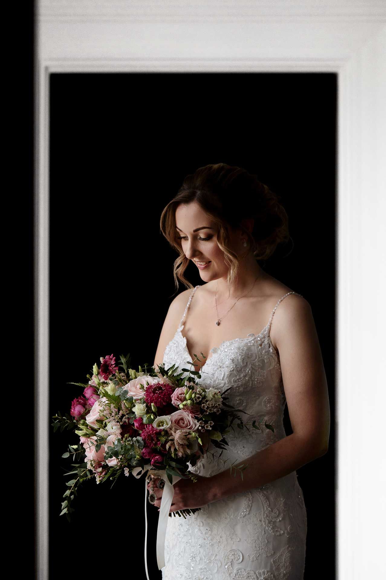 Sophie looking down at her beautiful pink flower bridal bouquet in her wedding dress. Photography by Fountain Photography. Videography by Veiled Productions.