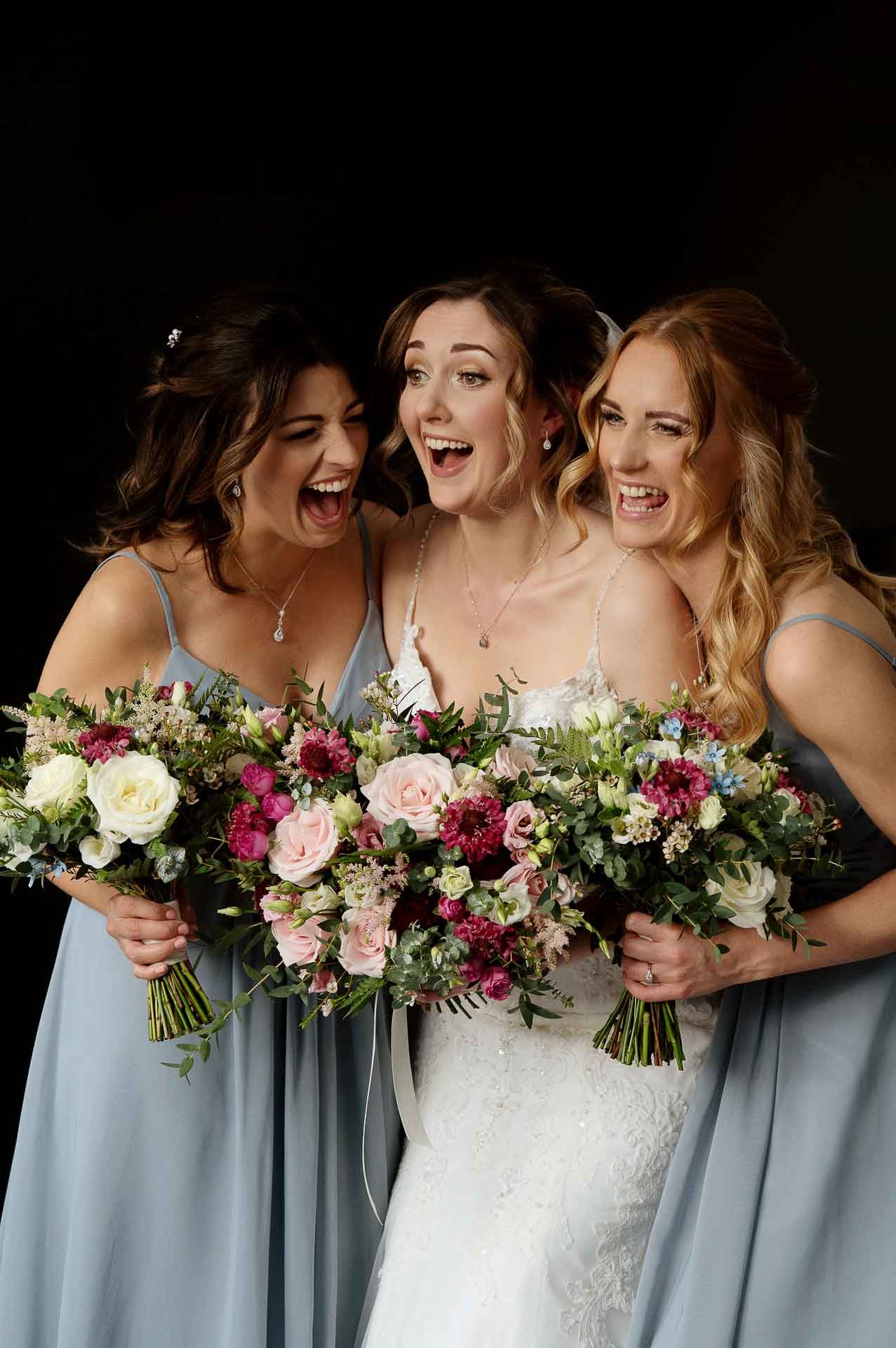 Sophie and her bridesmaids giggling holding their pink flower bouquets before the ceremony at Swynford Manor. Photography by Fountain Photography. Videography by Veiled Productions.