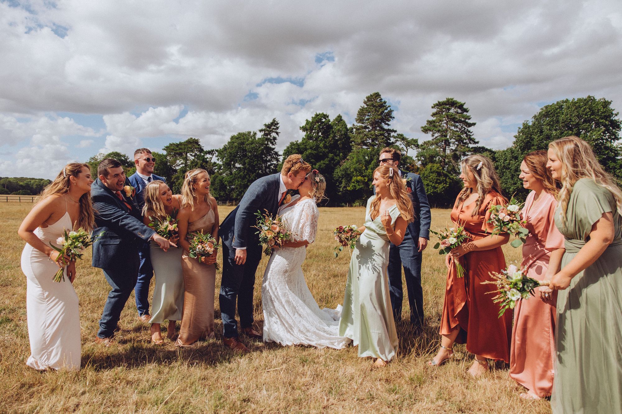 Nor and Dan's wedding party cheer as they share a kiss in the Buckinghamshire countryside. Photo thanks to Fordtography.