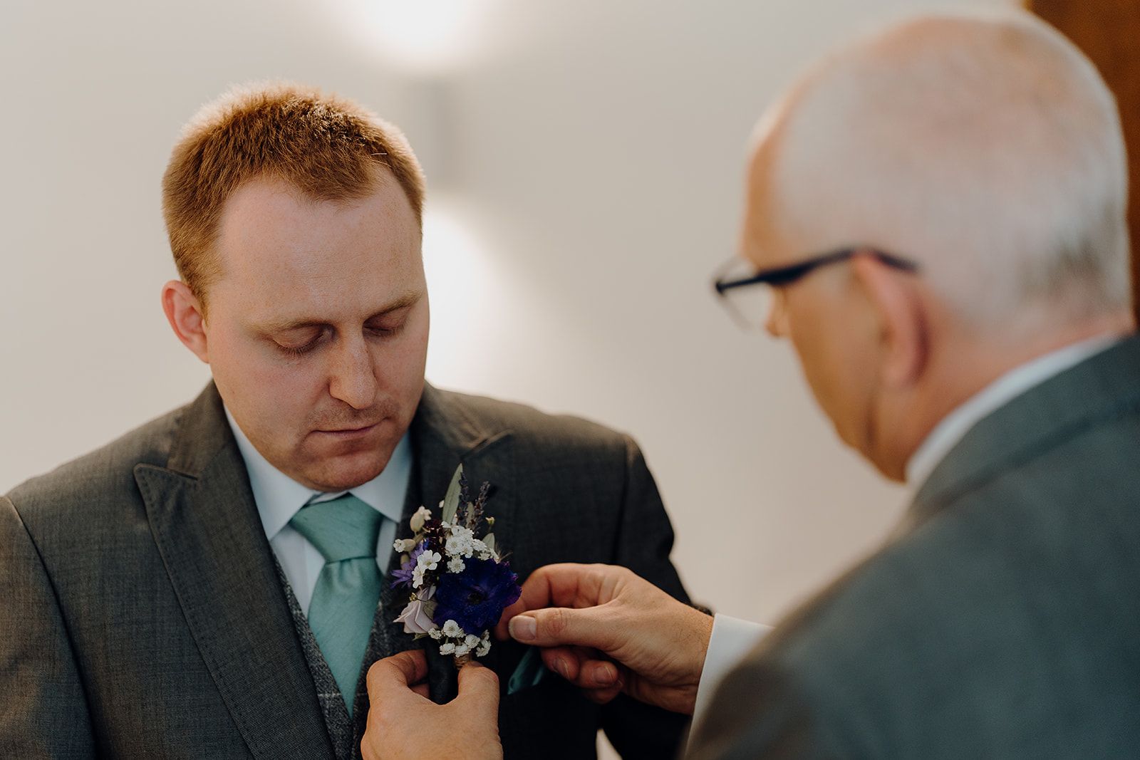 James' Dad attaching James' button hole to his jacket. Beautiful purple flowers with small daisies. Photo thanks to Sam and Steve Photography. 