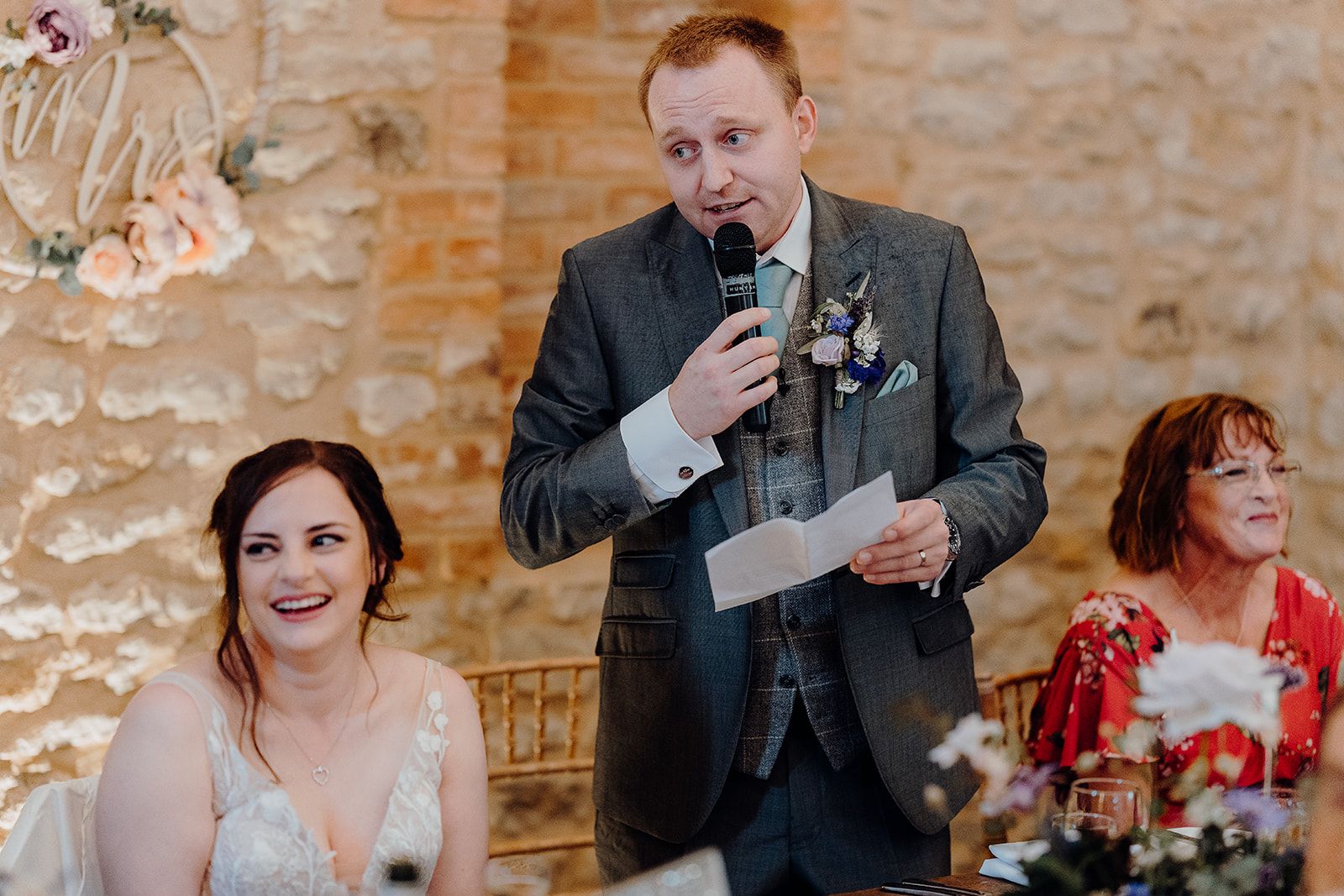 Groom James making his speech with Bride Georgie and Mother of the Bride laughing in the barn at Huntsmill Farm.