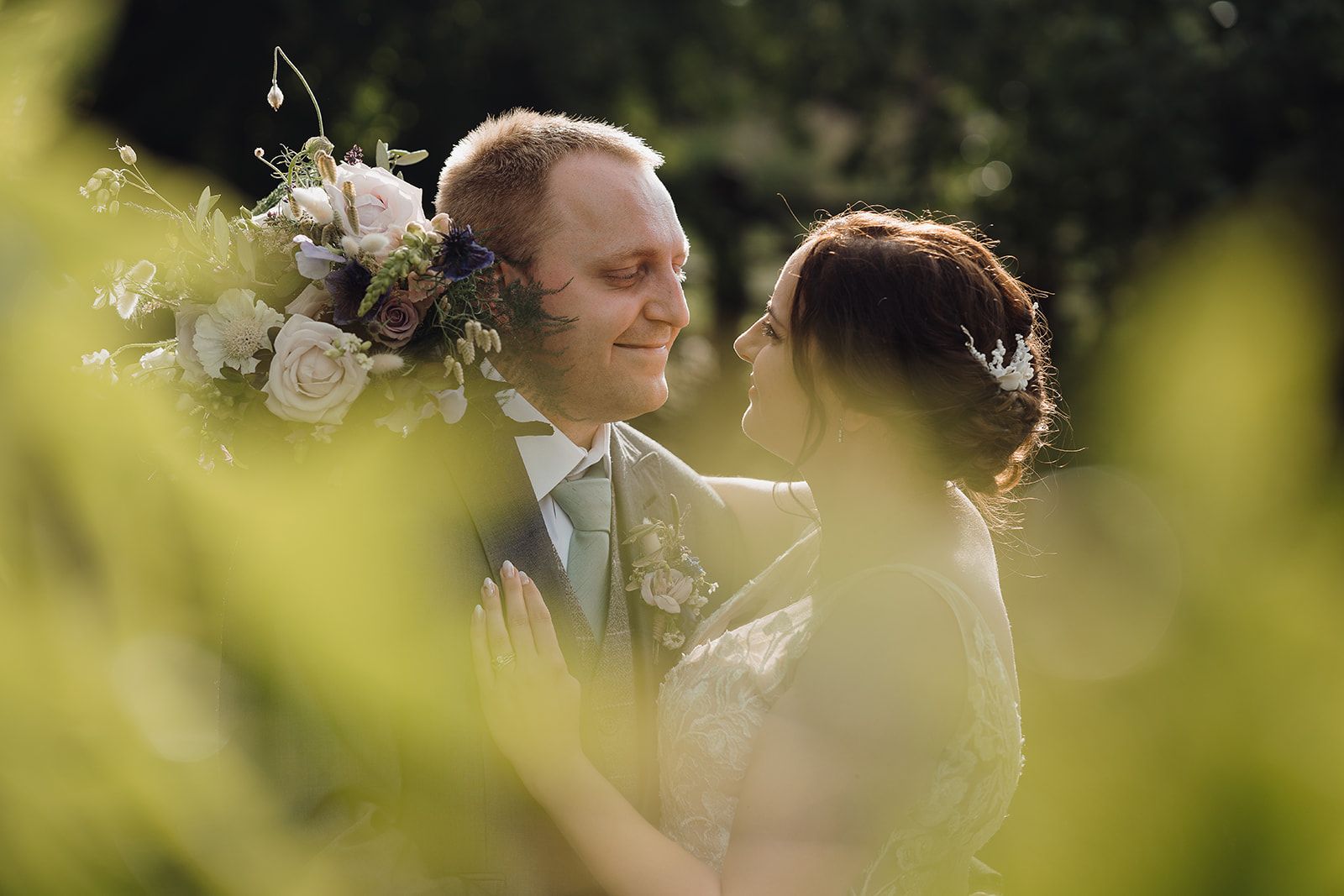 Beautiful photo shot through the leaves of a tree with Georgie and James looking at each other, Georgie holding her bouquet. Photo thanks to Sam and Steve Photography.