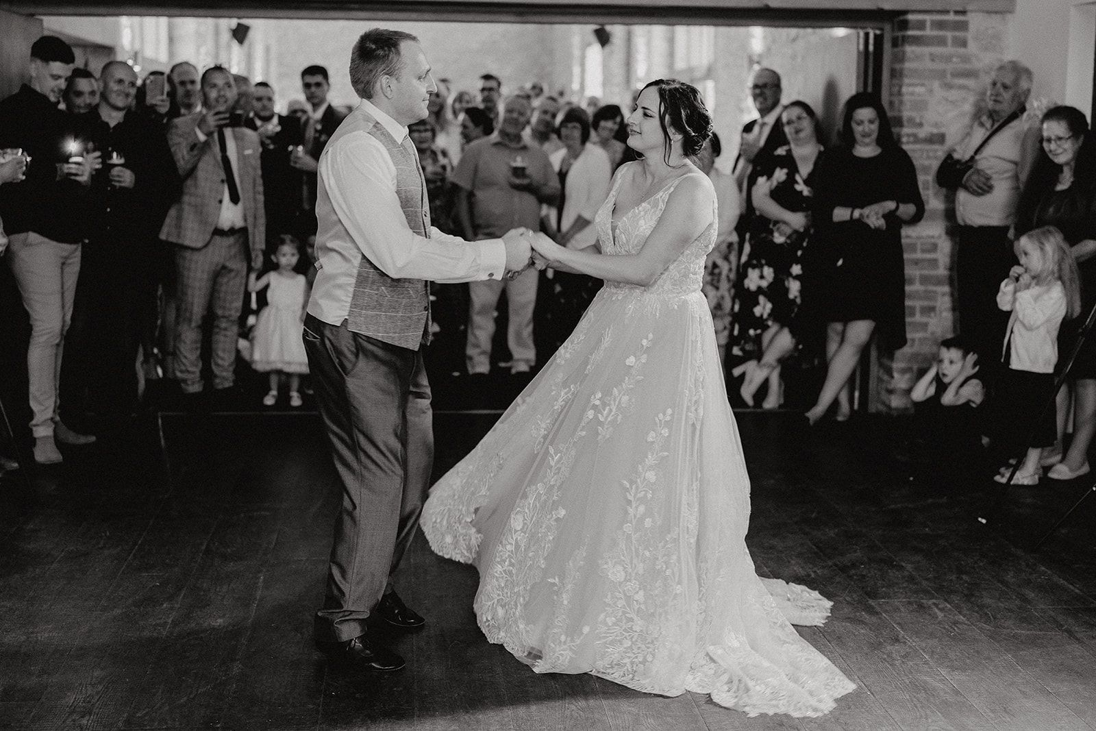 Georgie and James holding hands during their choreographed first dance with their guests watching in the background. Photo thanks to Sam and Steve Photography.