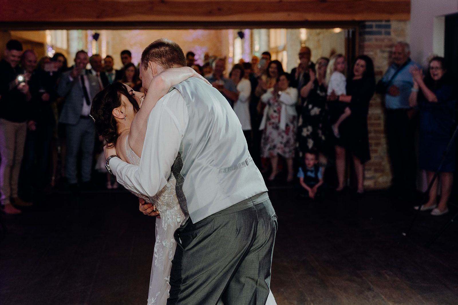 James holding Georgie in an embrace at the end of their choreographed first dance. All their guests are clapping in the background. Photo thanks to Sam and Steve Photography. 