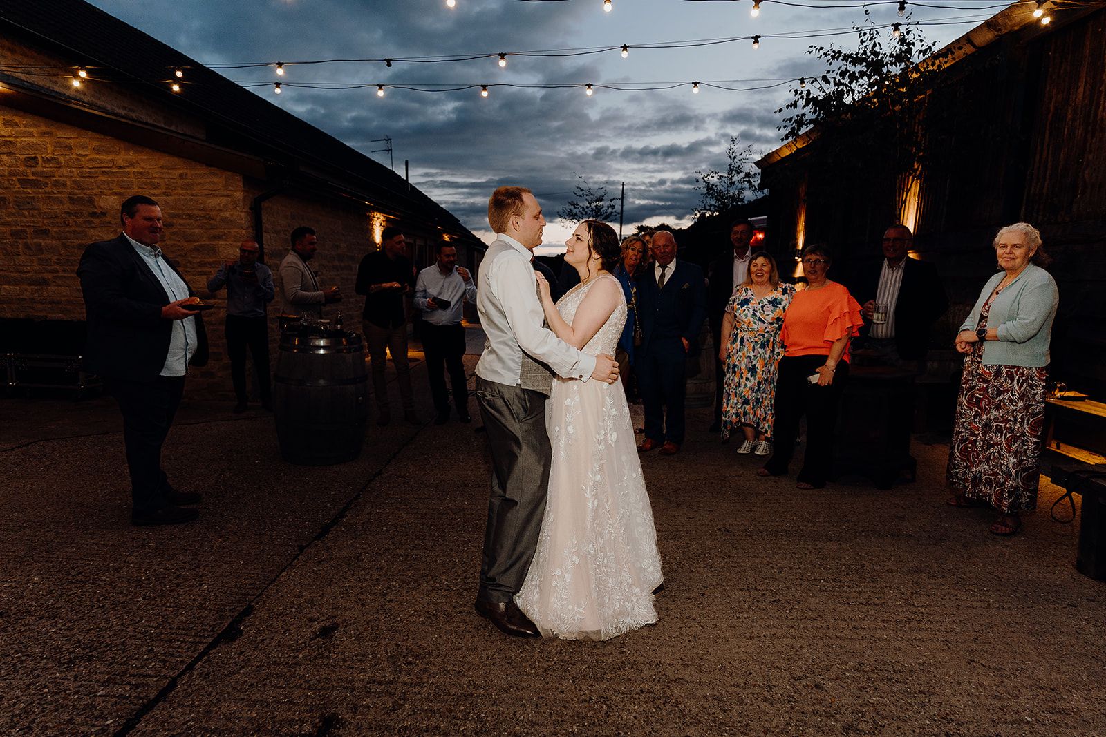Georgie and James embracing as it guests dark in the courtyard of Huntsmill Farm. Photo thanks to Sam and Steve Photography.