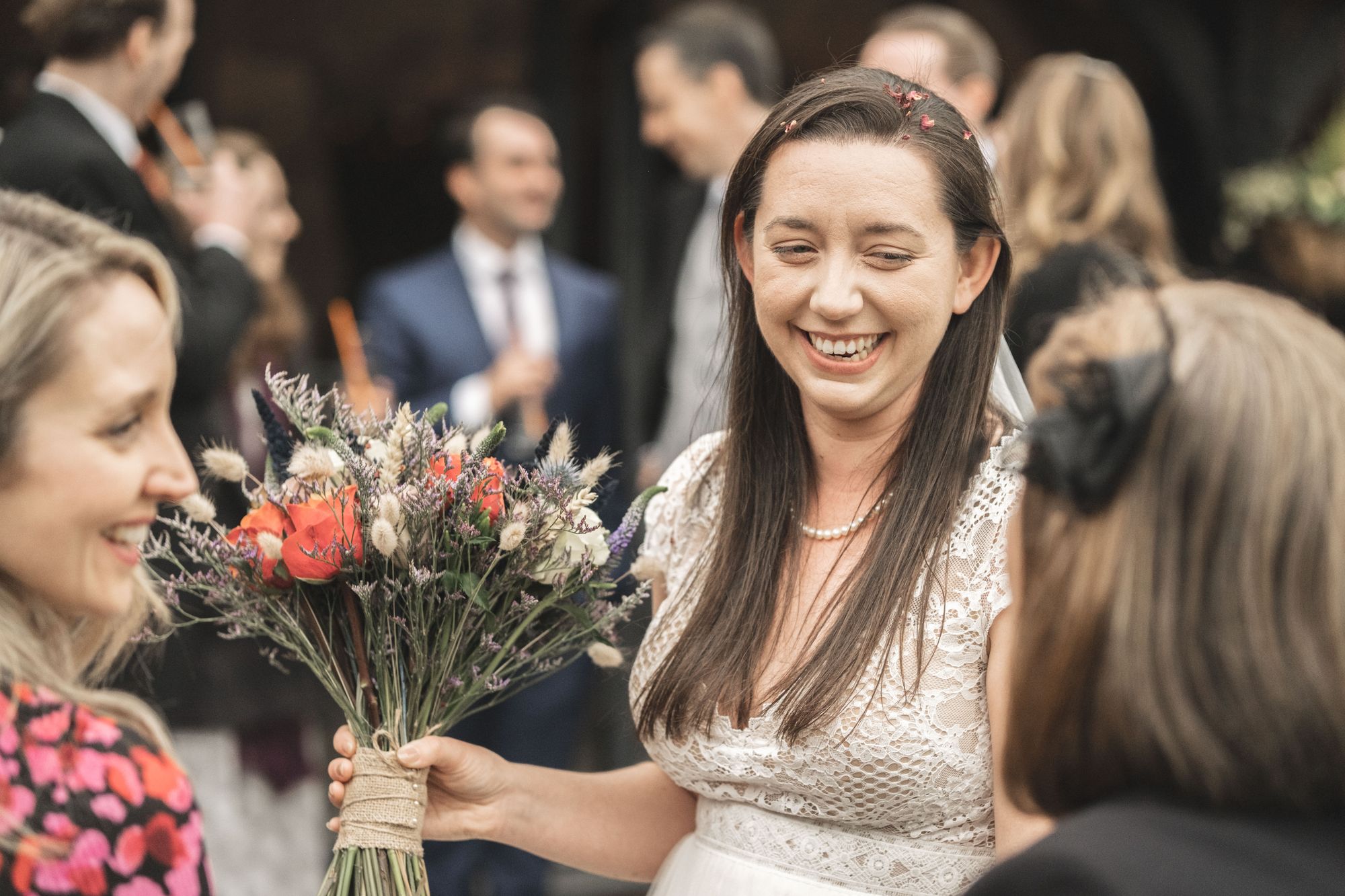 Jennifer smiling whilst chatting to wedding guests holding her beautiful bouquet from Ann Laing. Photo thanks to The Falkenburgs via Big Day Productions