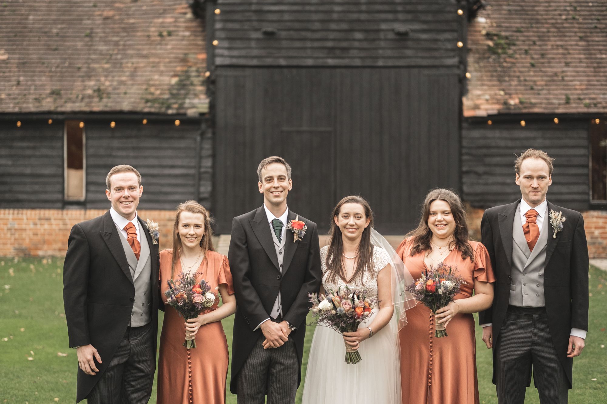 Newlyweds Jennifer and James stood with their bridesmaids and best men in front of the barn doors at Lains Barn in Oxfordshire. Photo thanks to The Falkenburgs via Big Day Productions