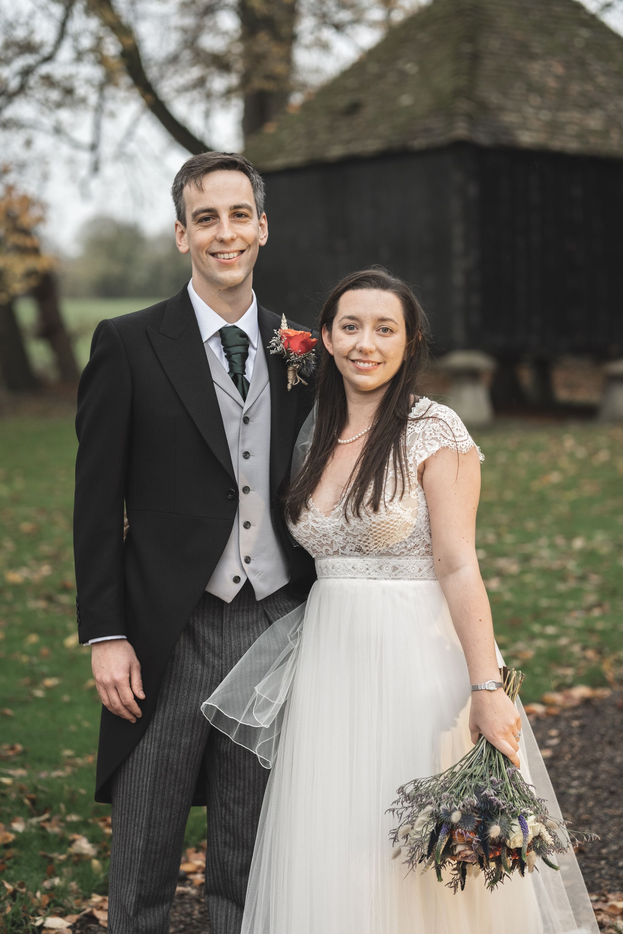 Jennifer and James smiling at the camera in front of the grain store at Lains Barn. Photo thanks to The Falkenburgs via Big Day Productions