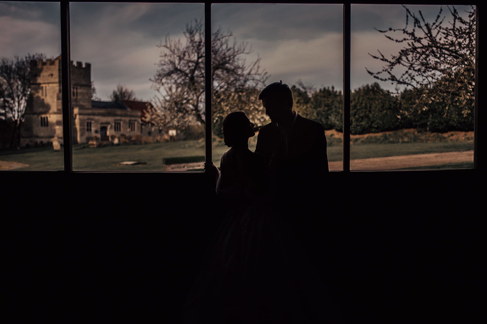 Gorgeous silhouette image of newlyweds from inside the barn with the trees and chapel in the grounds of Furtho Manor Farm in the background. Photo thanks to Francesca Checkley Photography.