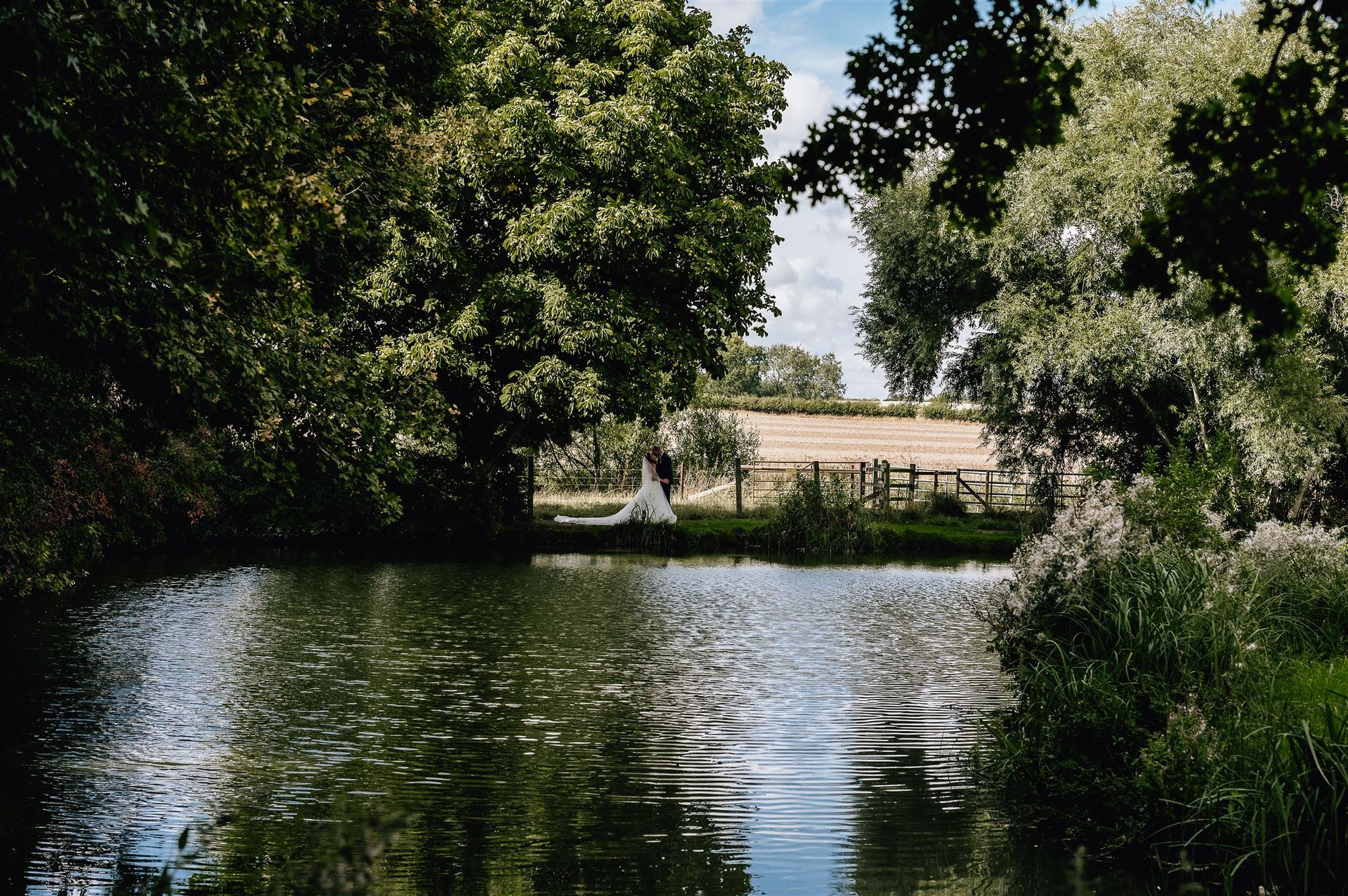 Newlyweds framed by trees across the lake at Furtho Manor Farm. Photo thanks to Francesca Checkley Photography.