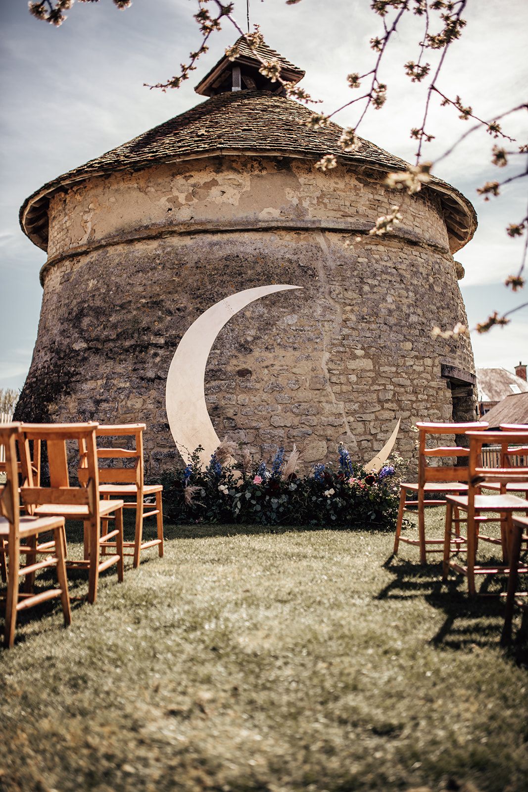 Wedding ceremony in front of the dovecot at Furtho Manor Farm with a gorgeous floral moon decoration at the front of the aisle. Photo thanks to Francesca Checkley Photography.