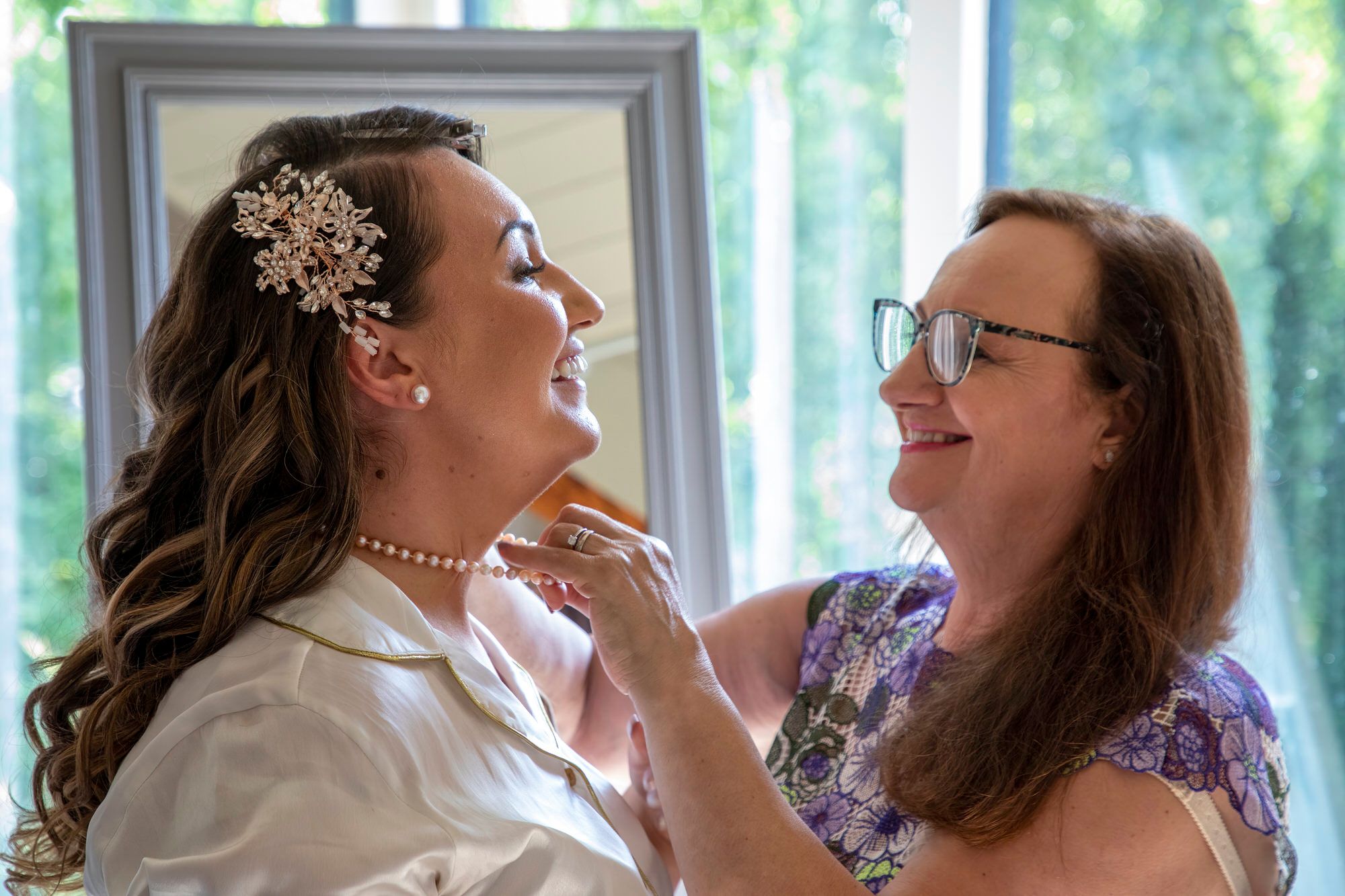 Joanna's Mum fastening Joanna's pearl necklace ahead of the wedding ceremony at South Farm in Cambridgeshire. Photo thanks to Nigel Charman Photography.