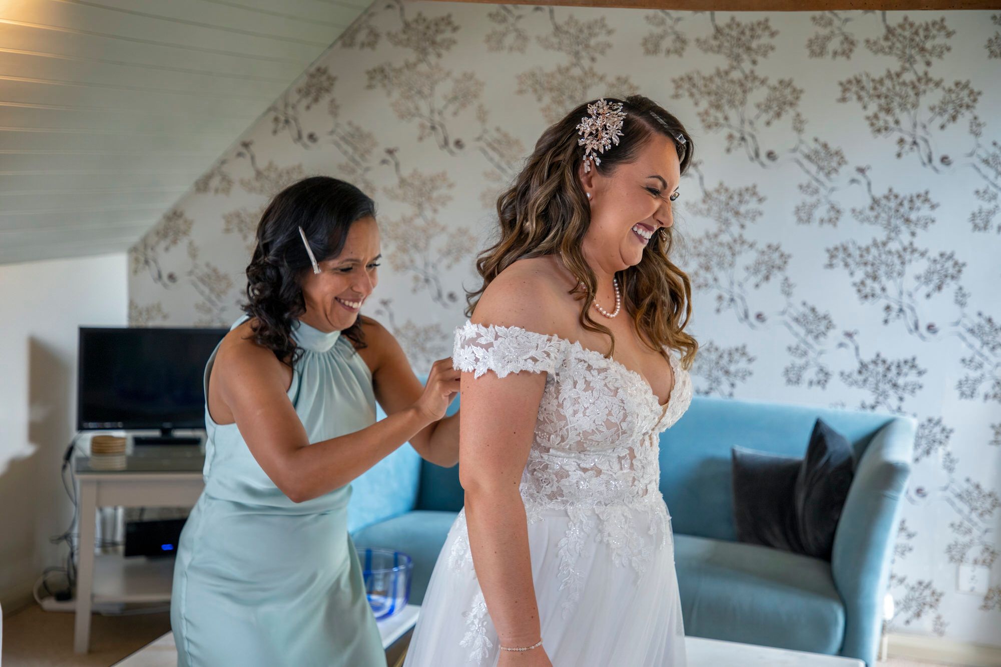Joanna's bridesmaid securing her wedding dress upstairs in the Coach House Suite at South Farm. Both ladies are smiling, very excited in the moment. Photo thanks to Nigel Charman Photography. 
