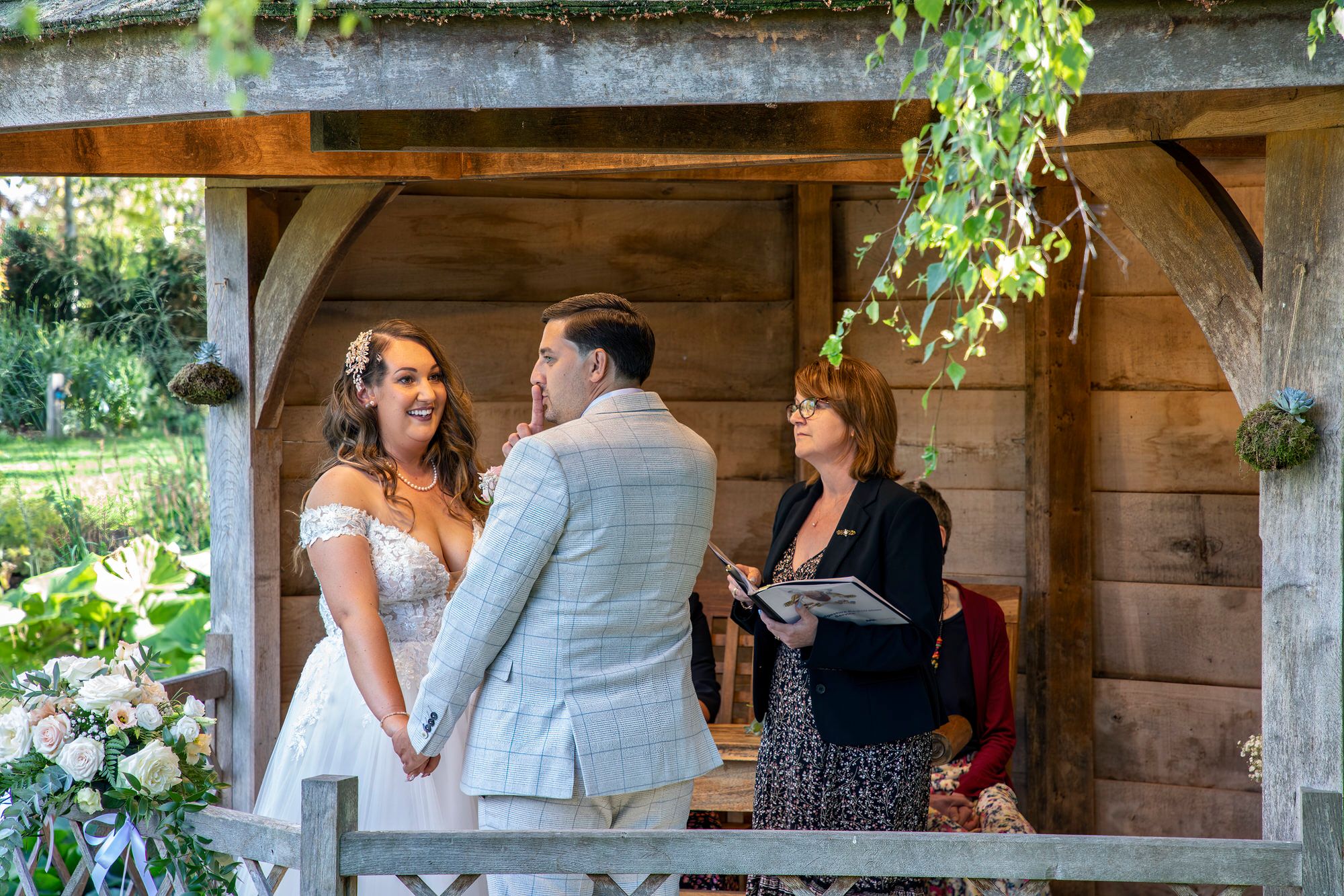 Rafal holding his finger to his lips to signal being quiet during the wedding ceremony when the registrar asks if anyone present knows any reason they shouldn't be married. Outdoor wedding ceremony in the Summer House at South Farm. Photo thanks to Nigel Charman Photography. 