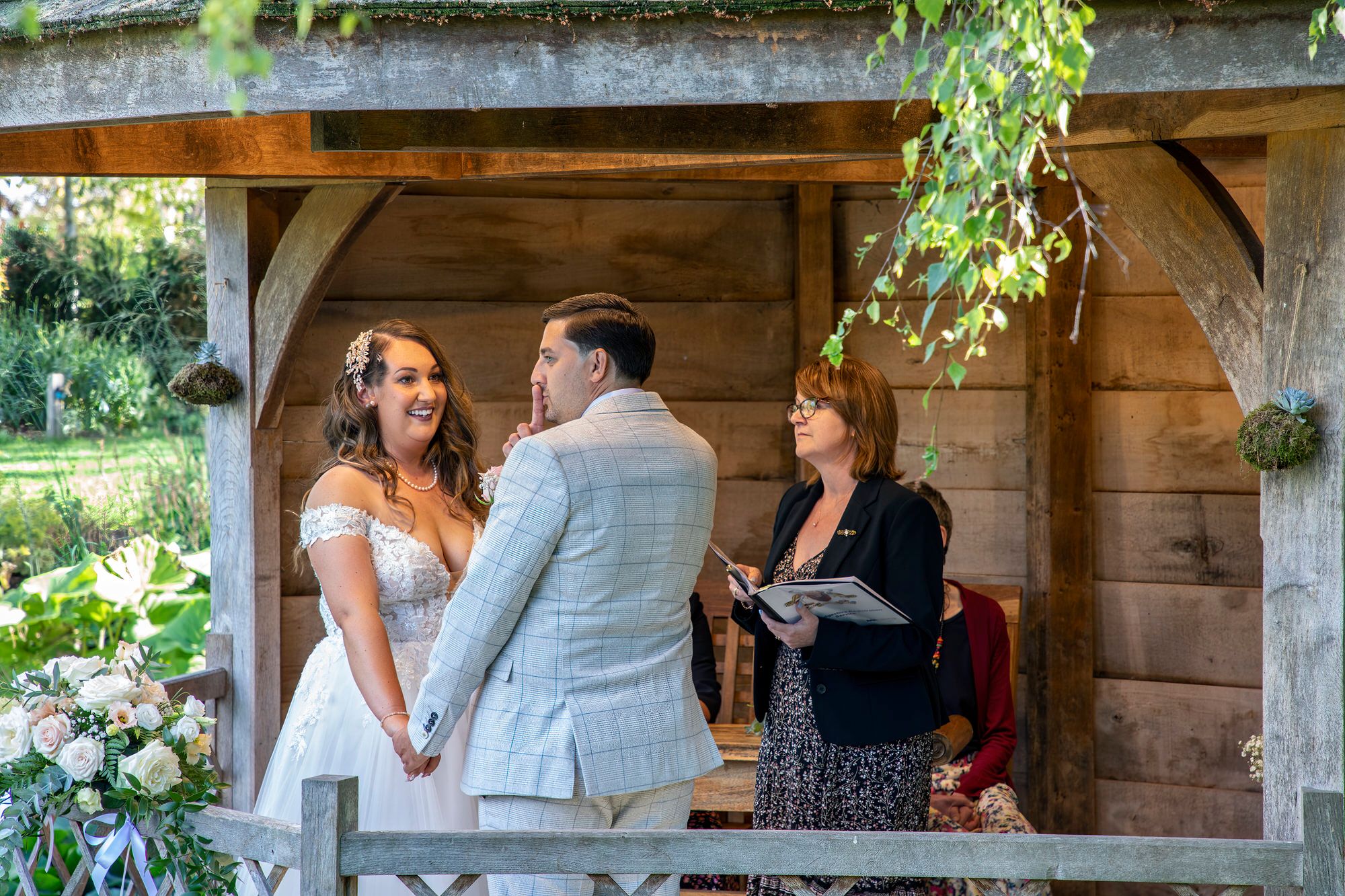Rafal holding his finger to his lips to signal being quiet during the wedding ceremony when the registrar asks if anyone present knows any reason they shouldn't be married. Outdoor wedding ceremony in the Summer House at South Farm. Photo thanks to Nigel Charman Photography.