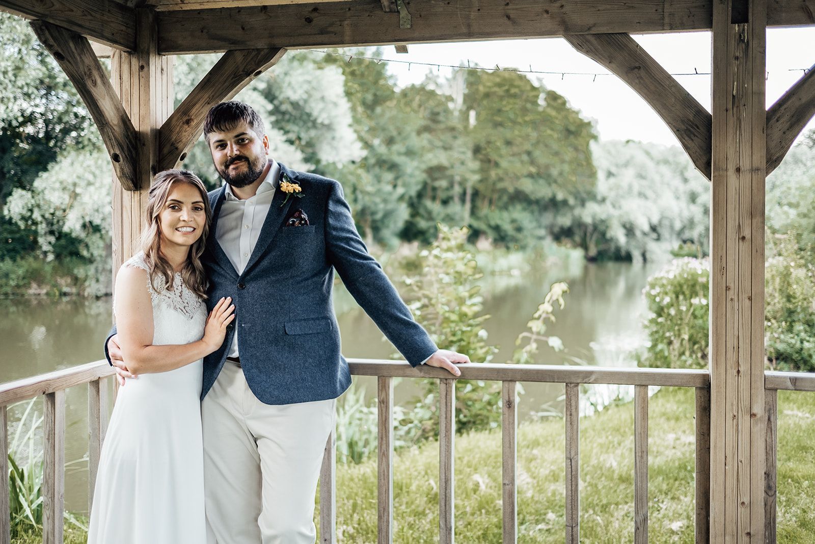 Newly weds stand in front of the lake under the gazebo smiling at the camera. Photo thanks to Francesca Checkley Photography.
