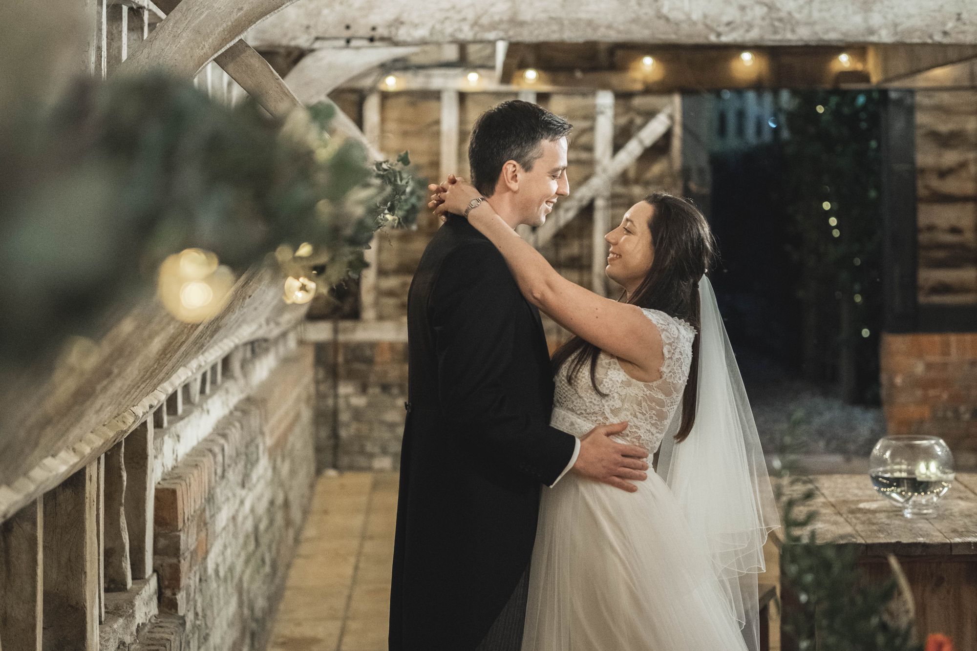 Jennifer and James under the covered byre at Lains Barn embracing under the twinkling lights. Photo thanks to The Falkenburgs via Big Day Productions