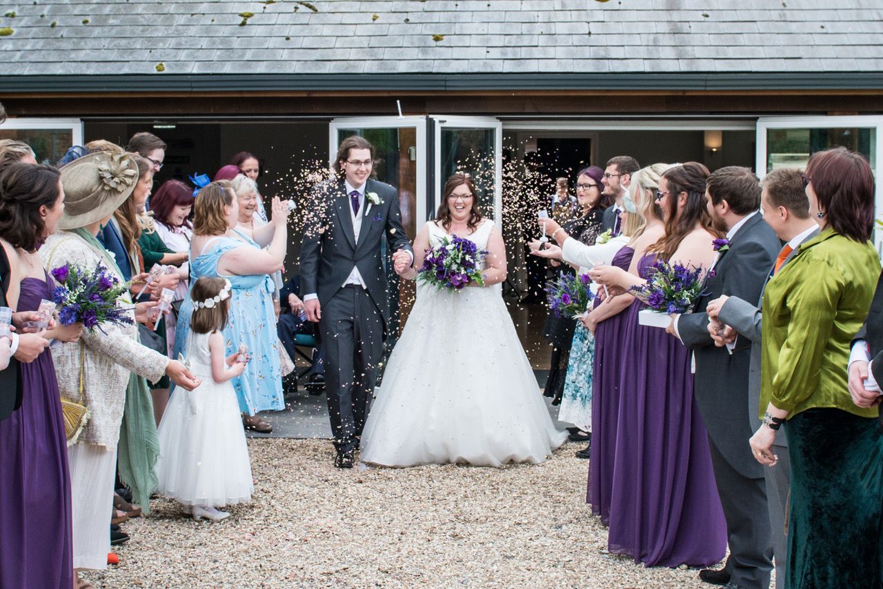 Kelly and Finn walk hand in hand as their guests throw confetti outside the Garden Barn at Wasing Park. Photo thanks to Zoe Warboys Photography.