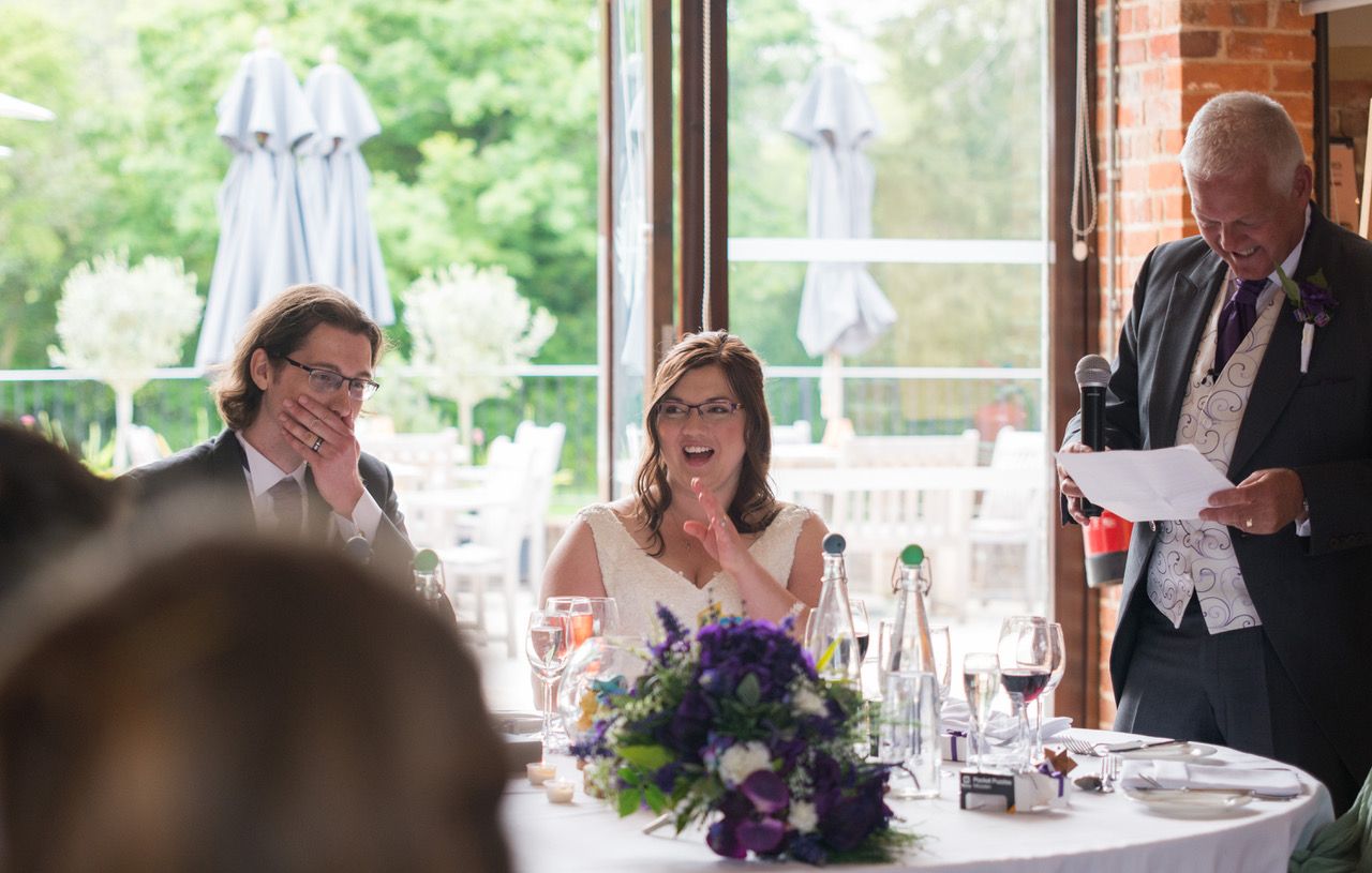 Kelly's Dad making his speech in the Castle Barn. Kelly is laughing and Finn has his hand over his mouth. Photo thanks to Zoe Warboys Photography at Wasing Park.
