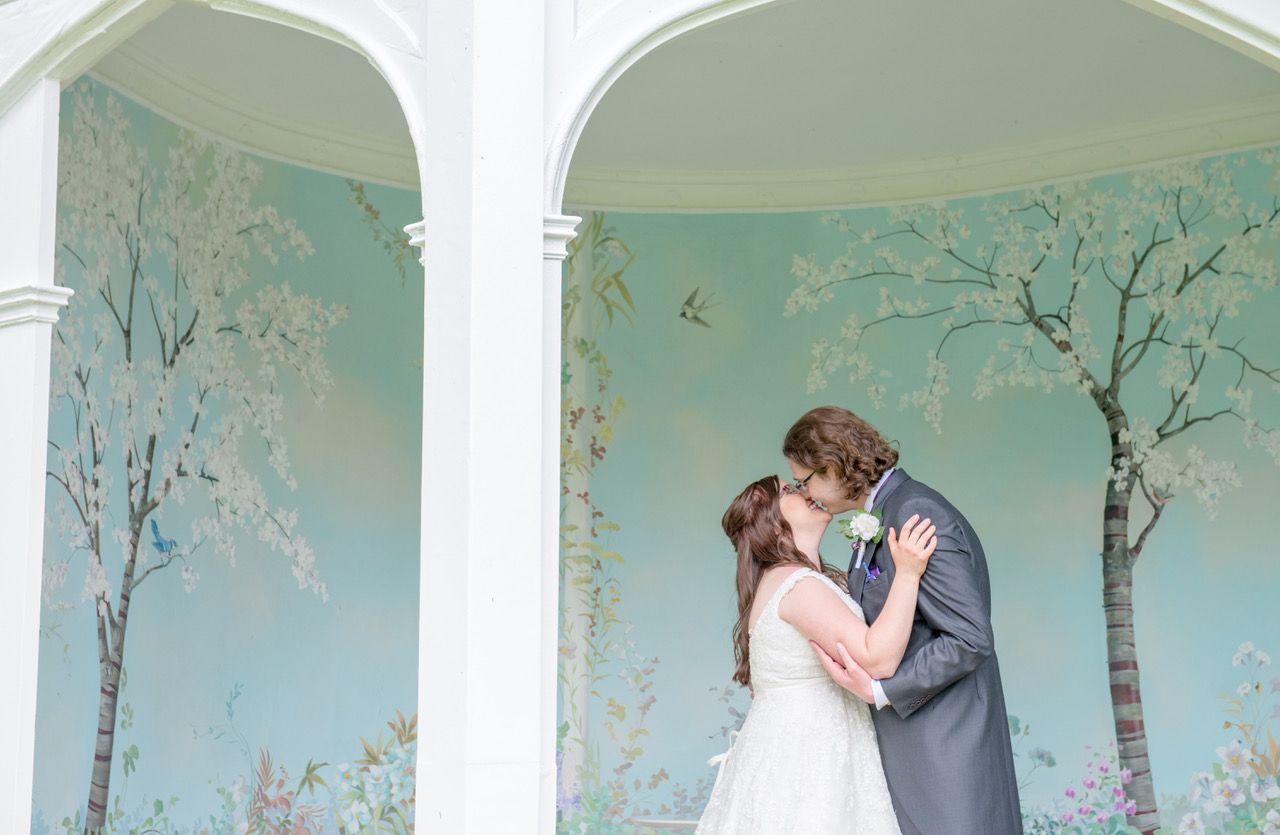 Kelly and Finn kissing in the Summerhouse at Wasing Park which has beautiful painted walls of blue sky and white bloosom trees. Photo thanks to Zoe Warboys Photography.