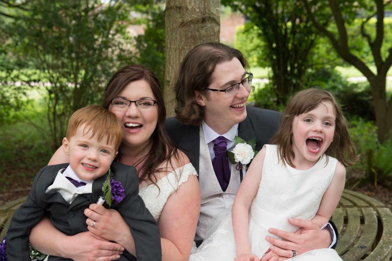 A natural family photograph in the woodland area of the gardens at Wasing Park. Kelly and Finn laugh with their two children sat on their laps. Photo thanks to Zoe Warboys Photography.